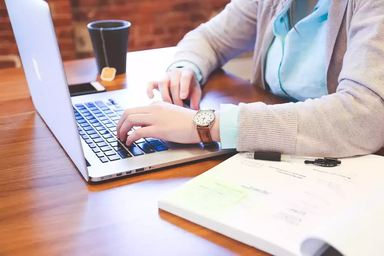Eine Person arbeitet neben Sachbuch und Kaffee am Laptop.
